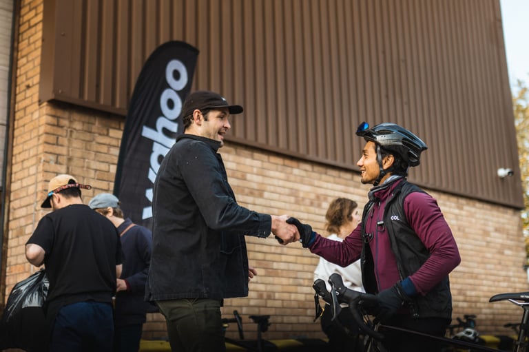 Rider in a helmet shakes hands with a man in a cap beside a Wahoo feather flag at the Gravel Bonanza start in Wilmslow.