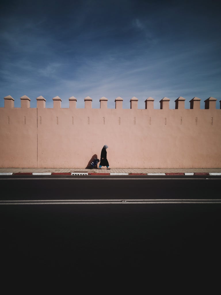 Pink crenellated rampart wall in Marrakech, a figure walking the pavement below it before the Atlas Mountain Race.