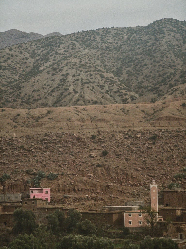 Mud-brick village and pink minaret beneath barren, scrub-dotted hillsides on day one of the Atlas Mountain Race.