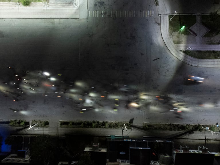 Aerial night view of Silk Road Mountain Race riders' lights blurring along a city street at the start.