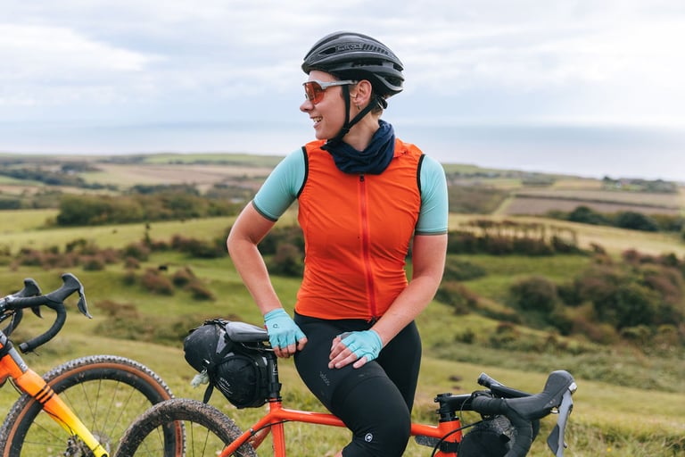 Claire Frecknall pauses on her orange gravel bike with a bar bag above Isle of Wight farmland.