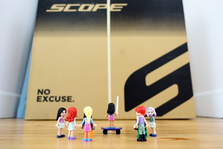 Toy figures stand before the Scope shipping box printed with 'No Excuse' as the R4A wheels arrive.