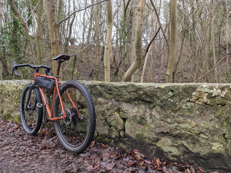 Orange Fairlight Secan with a StraightCut Design frame bag leaning on a stone wall in bare winter woodland.