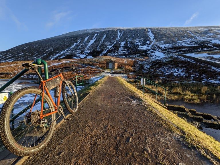 Fairlight Secan leaning on green railings on a reservoir track, snow-streaked hillside beyond, en route to Black Hill.