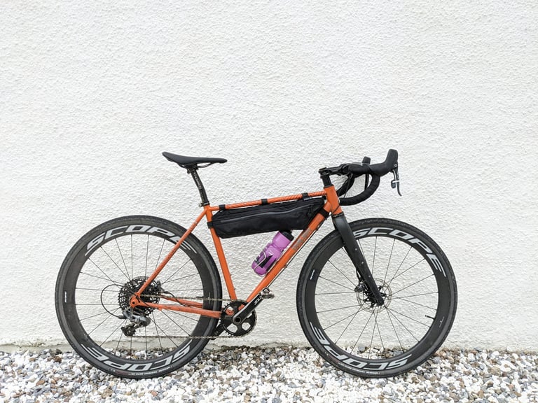 Orange Fairlight Secan with Scope carbon wheels and a frame bag against a white wall at Polin.