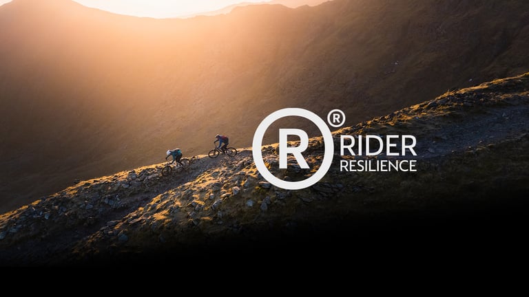 Rider Resilience logo over two mountain bikers climbing a sunlit ridge trail.