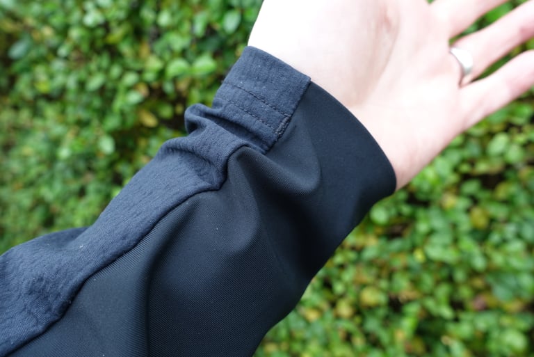 Stretchy black Lycra cuff of the POC Mantle hoodie sleeve at the wrist, against a hedge.